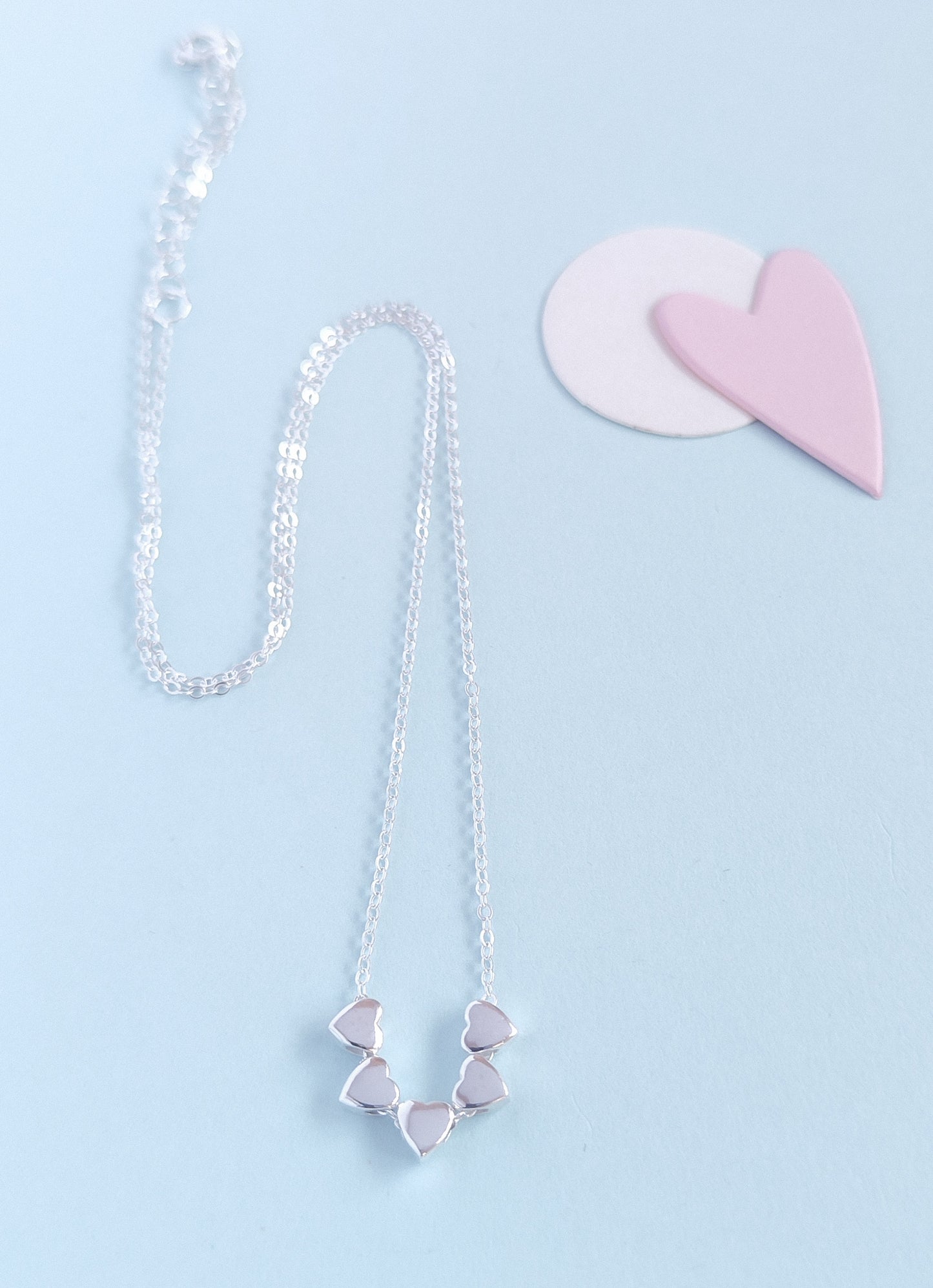 Silver necklace with heart-shaped pendants on a light blue background