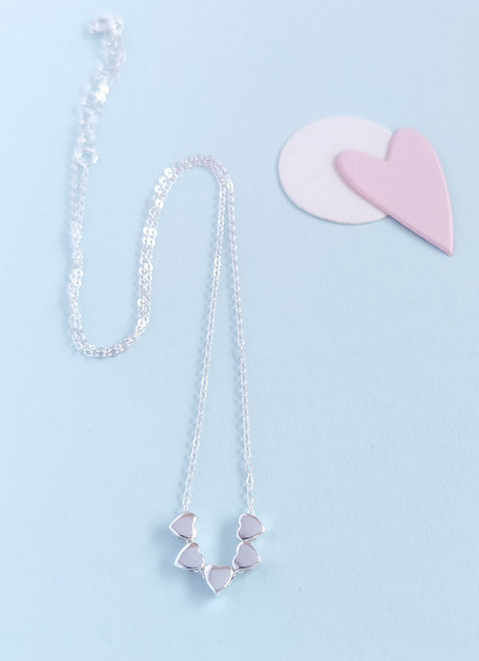 Silver necklace with heart-shaped pendants on a light blue background