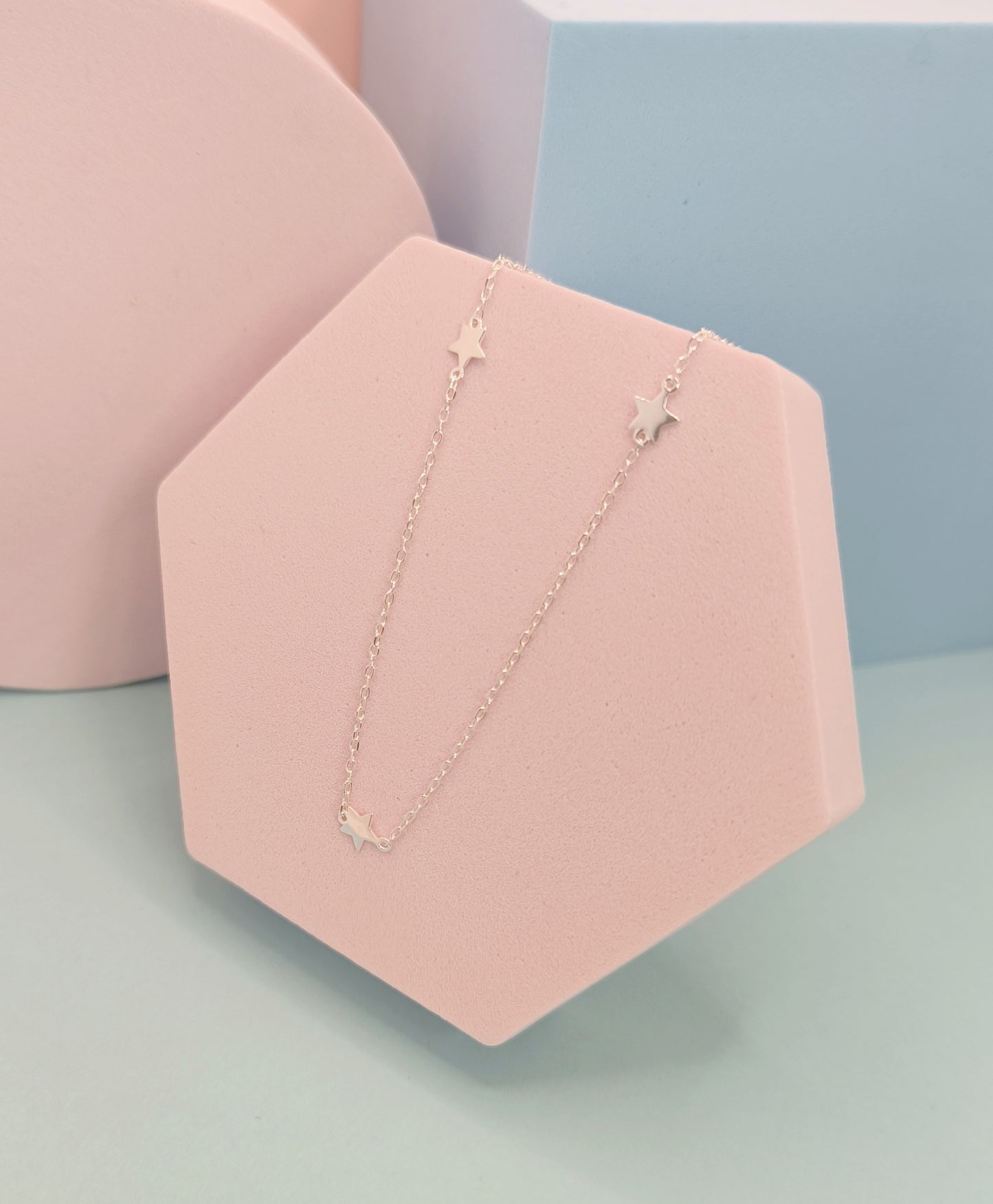 Necklace with star pendants on a pink stand against a light blue background