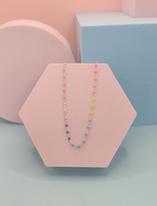 Colorful beaded necklace on a pink hexagonal stand with a pastel background