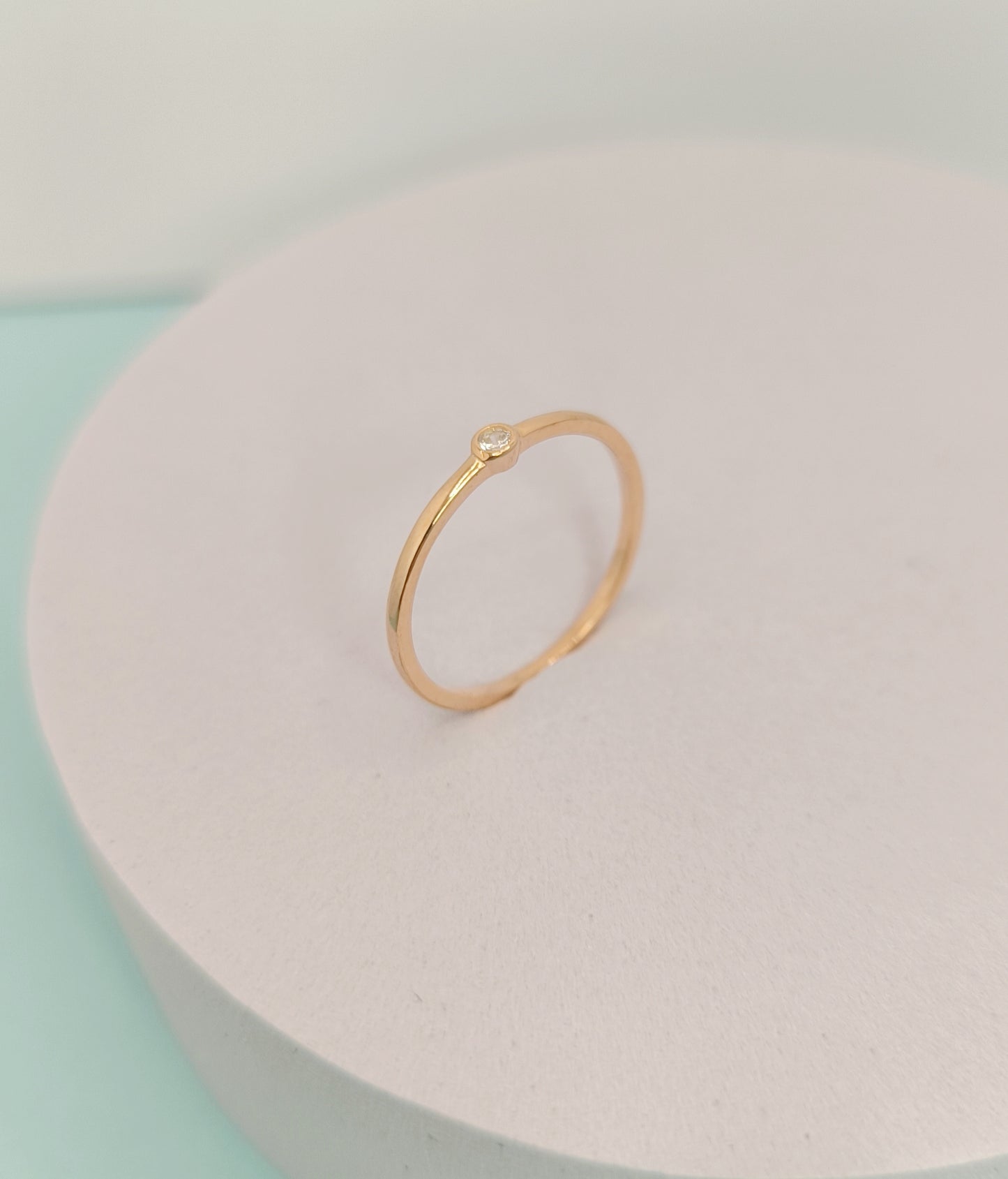 Gold ring on a light pink stand with a soft pastel background