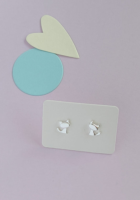 Silver dog-shaped earrings on a gray card with a light purple background