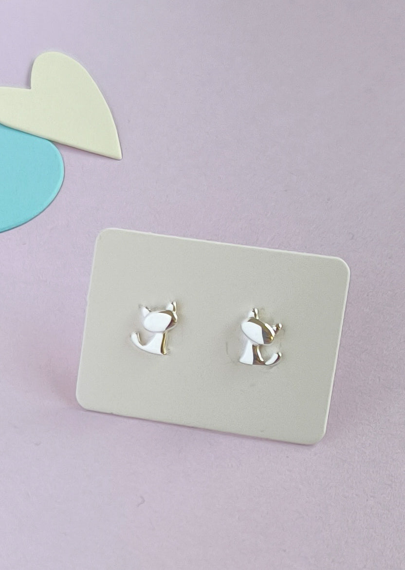 Cat-shaped earrings on a light gray card with a pastel purple background