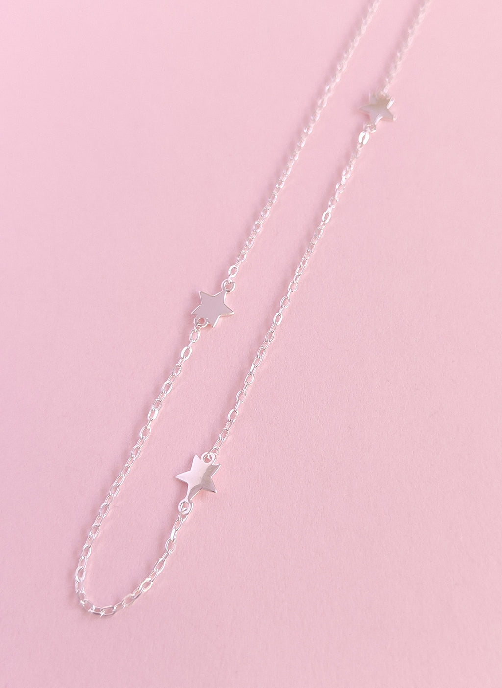 Silver chain necklace with star pendants on a pink background