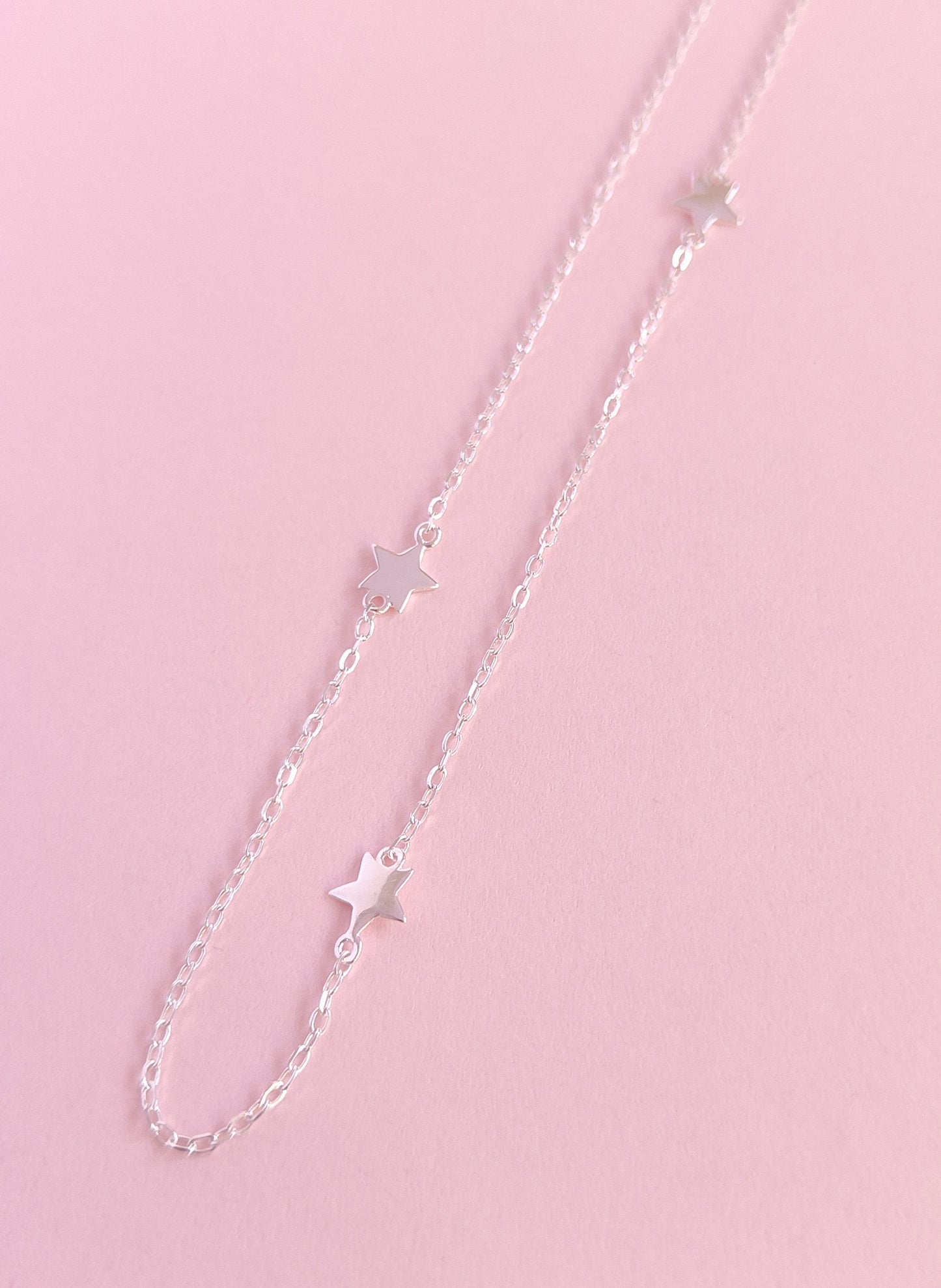 Silver chain necklace with star pendants on a pink background