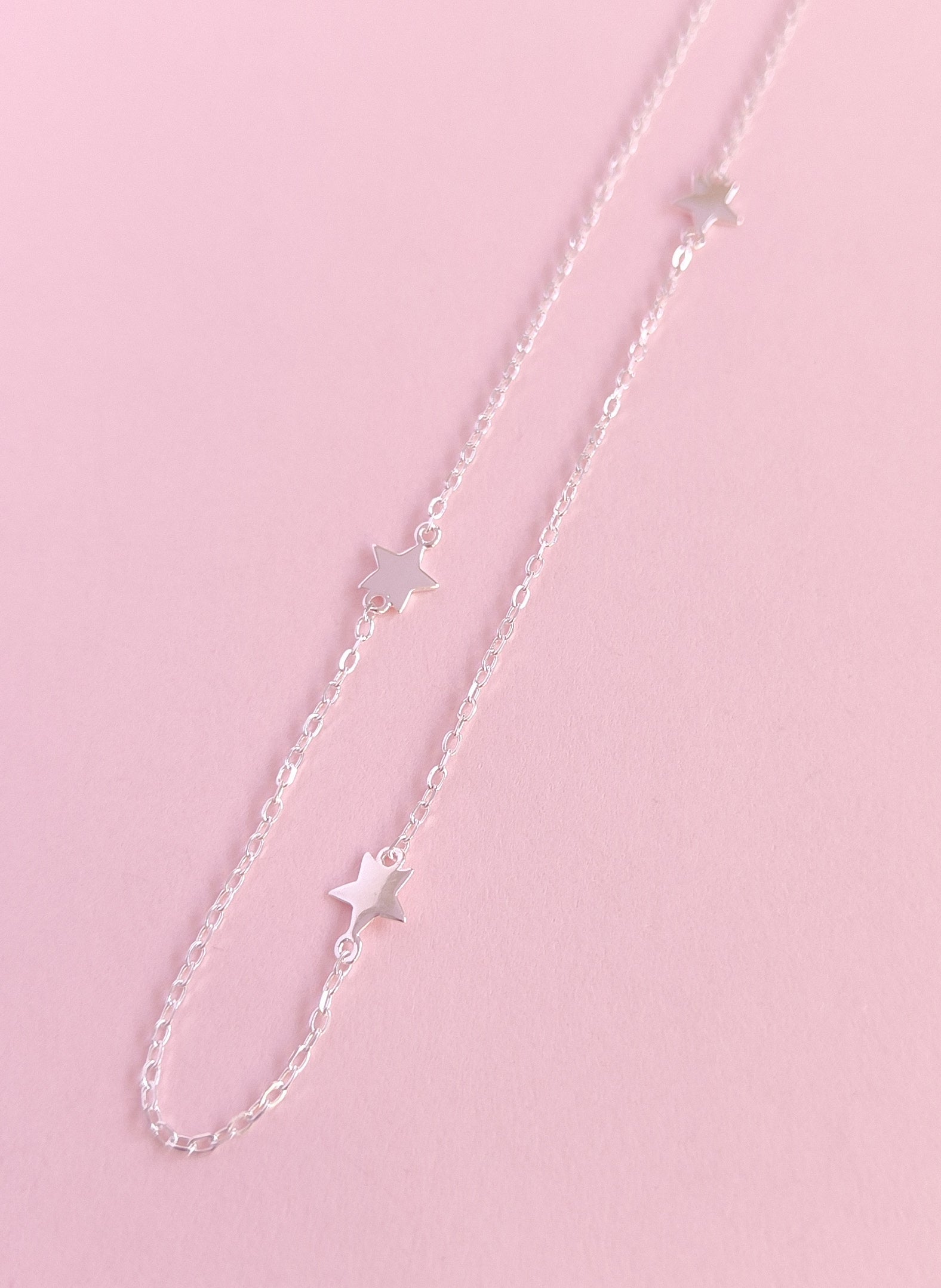 Silver chain necklace with star pendants on a pink background