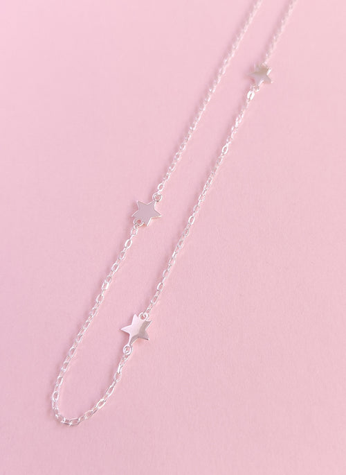 Silver chain necklace with star pendants on a pink background