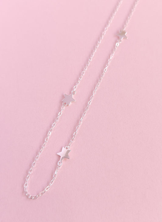 Silver chain necklace with star pendants on a pink background
