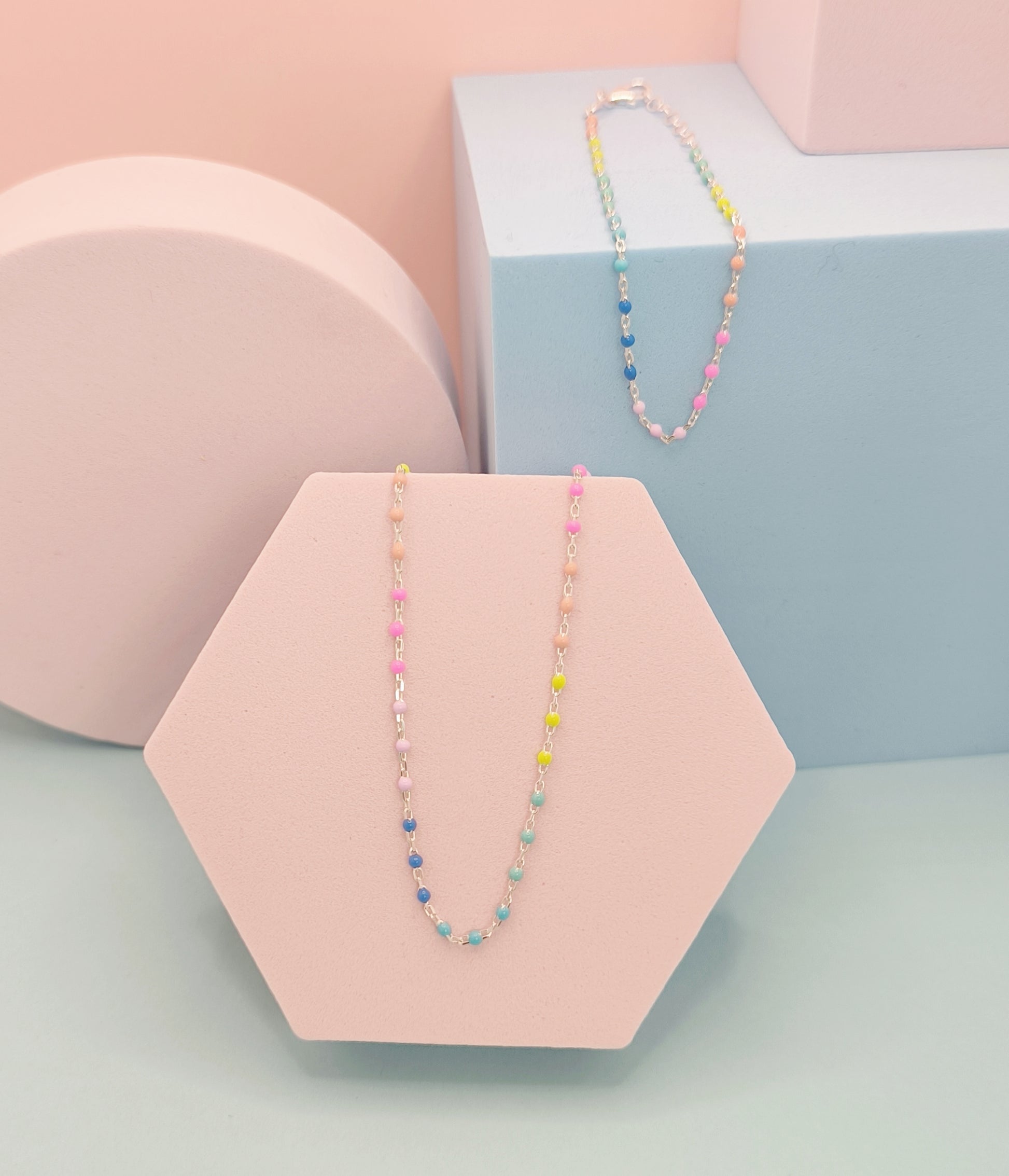 Colorful beaded necklace on a pink hexagonal stand with a pastel background
