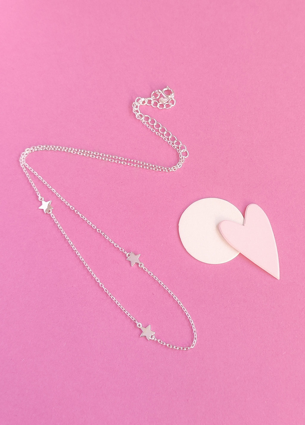 Silver necklace with star pendants on a pink background