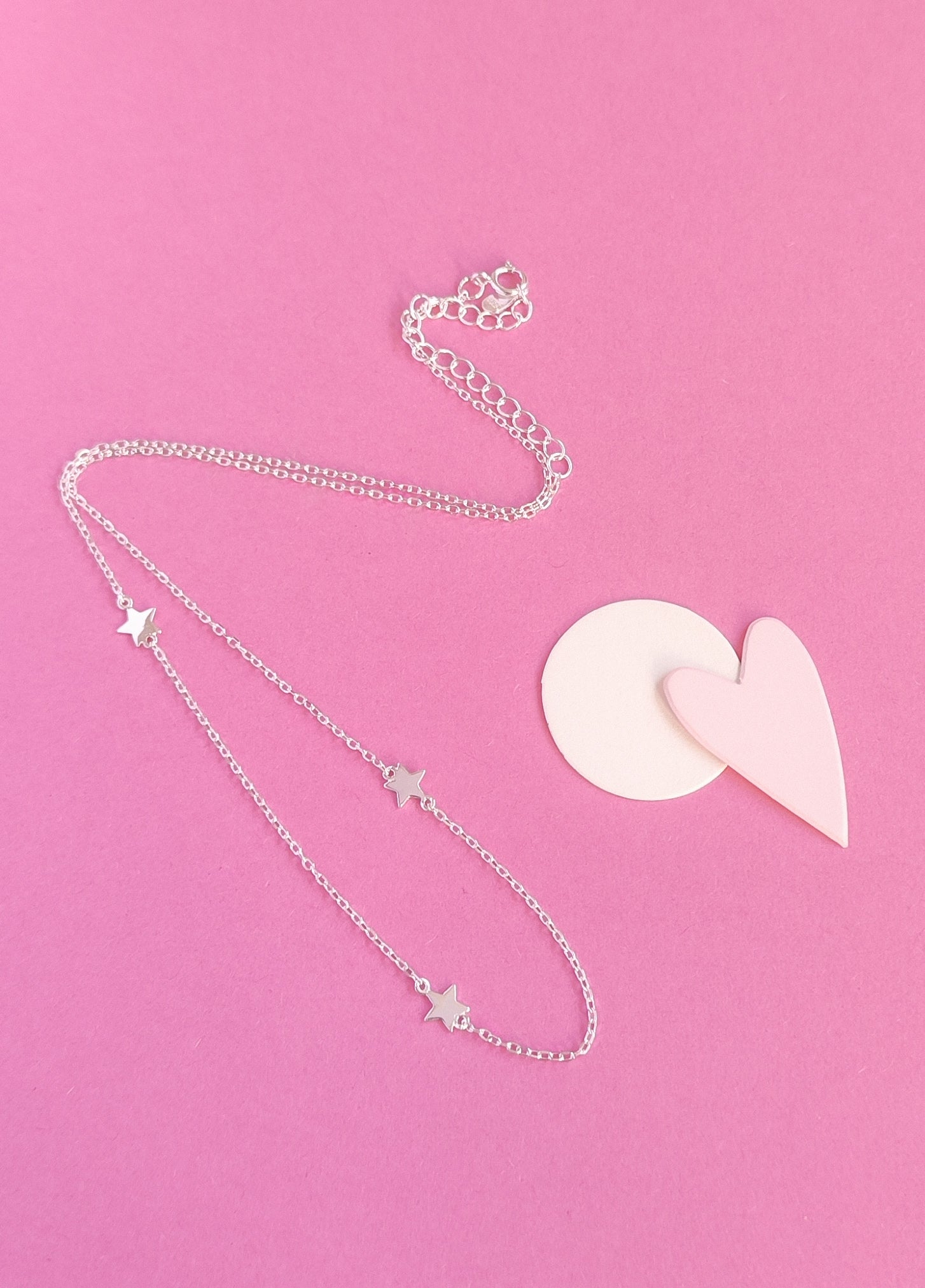 Silver necklace with star pendants on a pink background