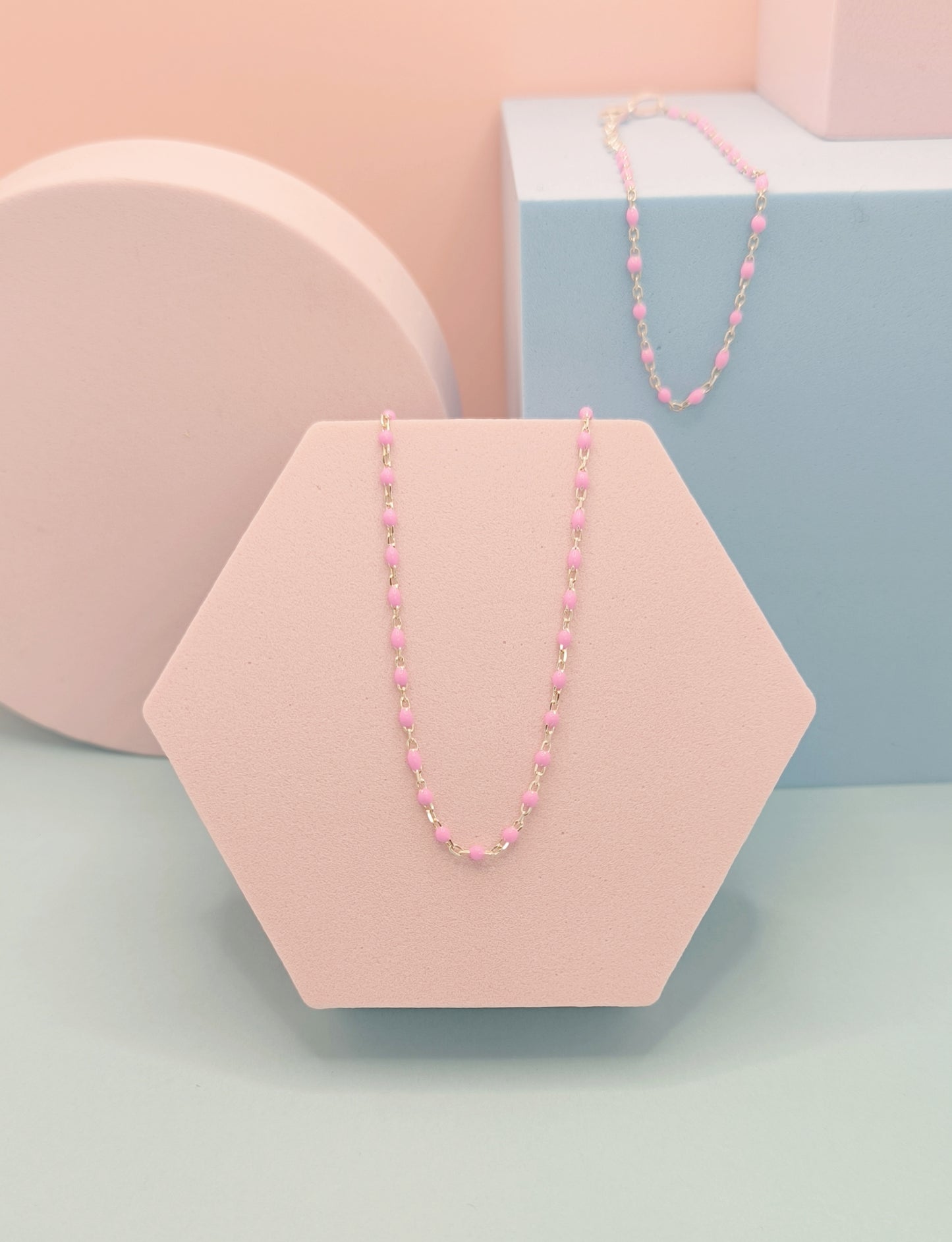 Pink beaded necklace on a hexagonal pink stand with a pastel background