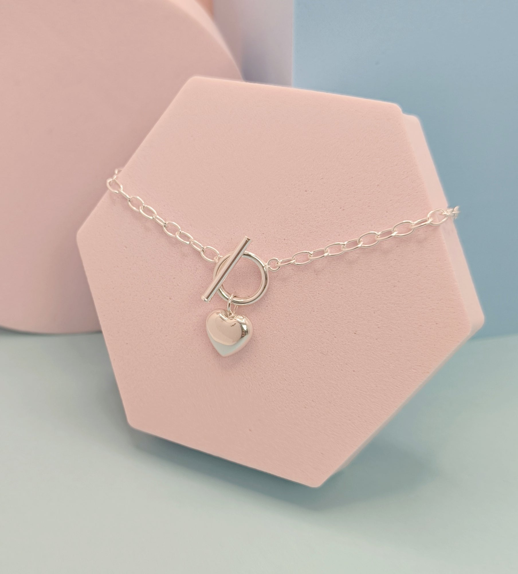 Necklace with a heart charm and letter 'P' on a pink stand against a light blue background