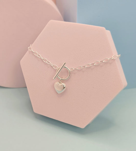 Necklace with a heart charm and letter 'P' on a pink stand against a light blue background