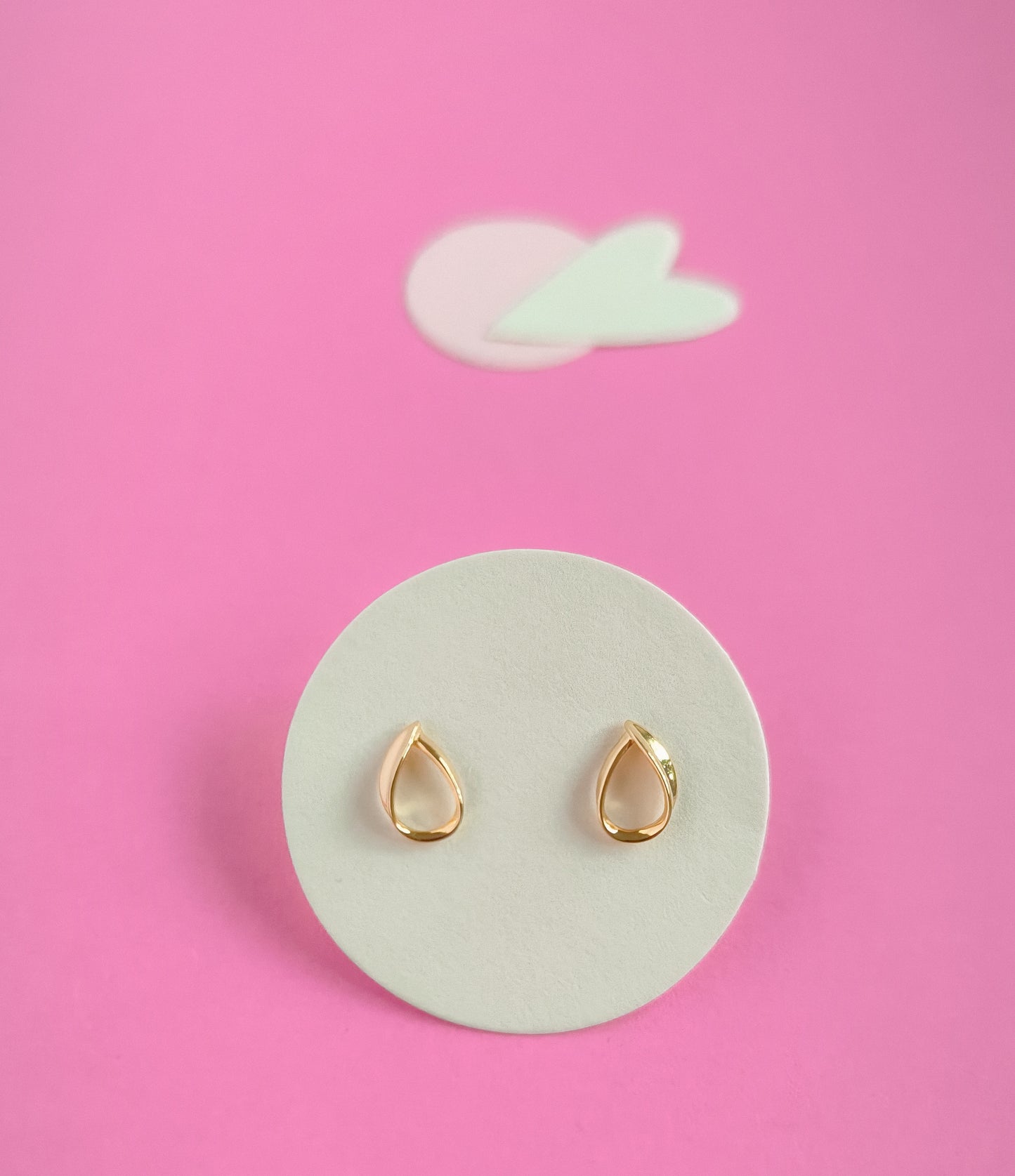 Gold teardrop earrings on a white circular pad with a pink background