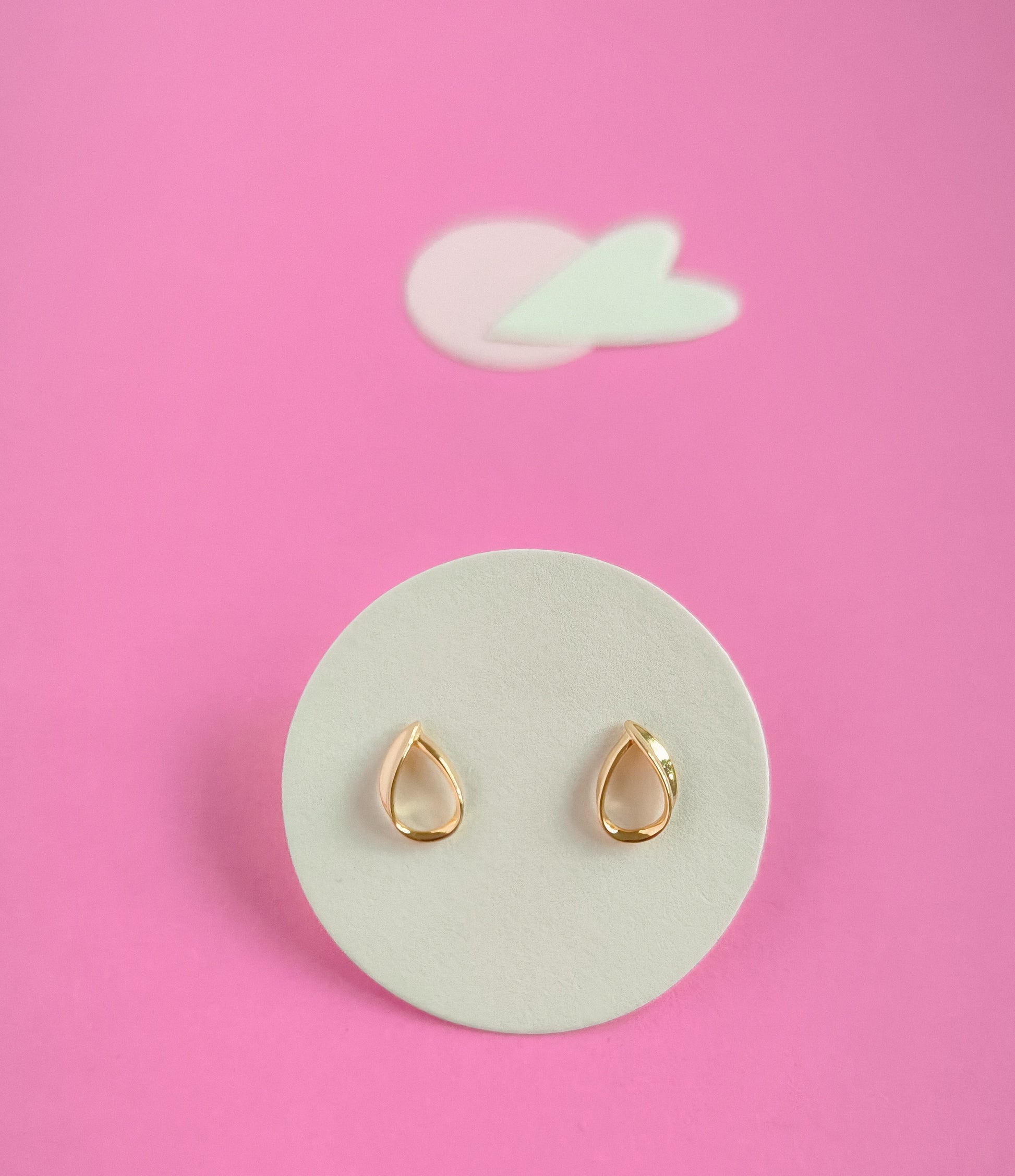 Gold teardrop earrings on a white circular pad with a pink background