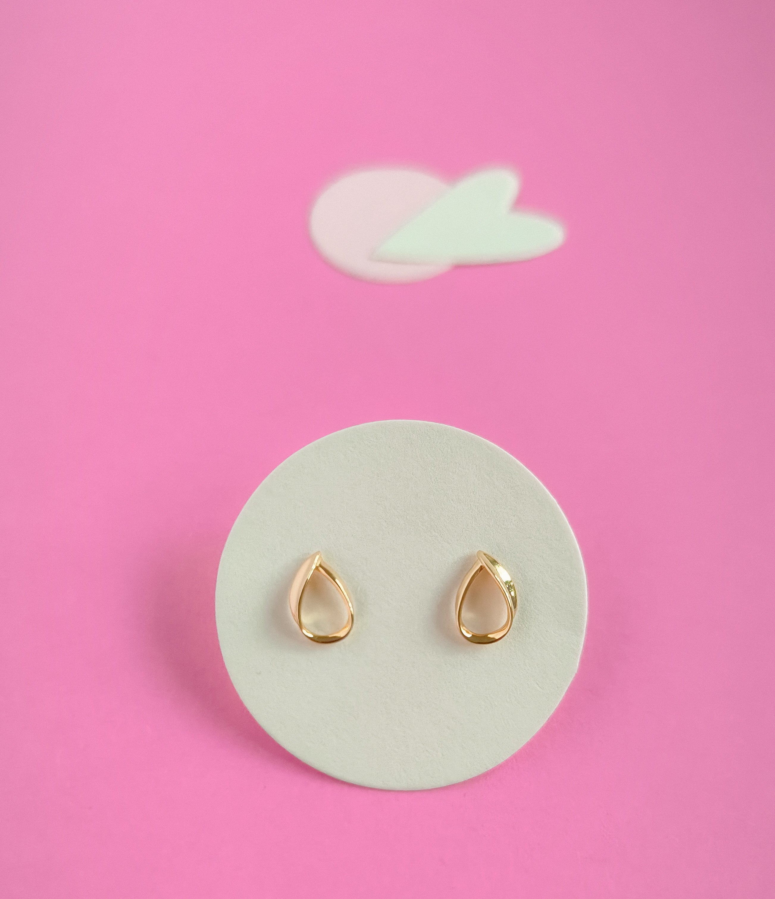 Gold teardrop earrings on a white circular pad with a pink background
