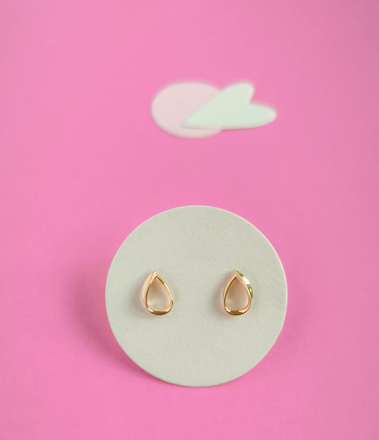 Gold teardrop earrings on a white circular pad with a pink background
