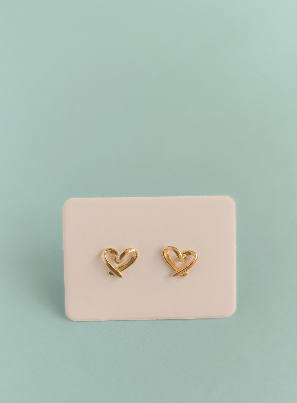 Gold heart-shaped earrings on a pink card against a light green background