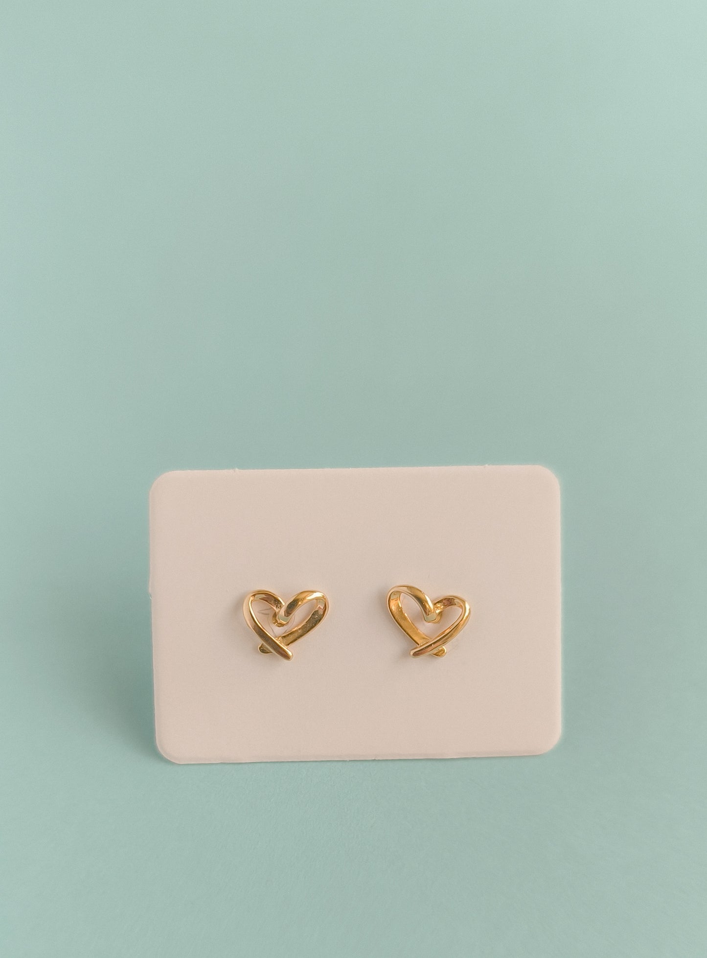 Gold heart-shaped earrings on a pink card against a light green background