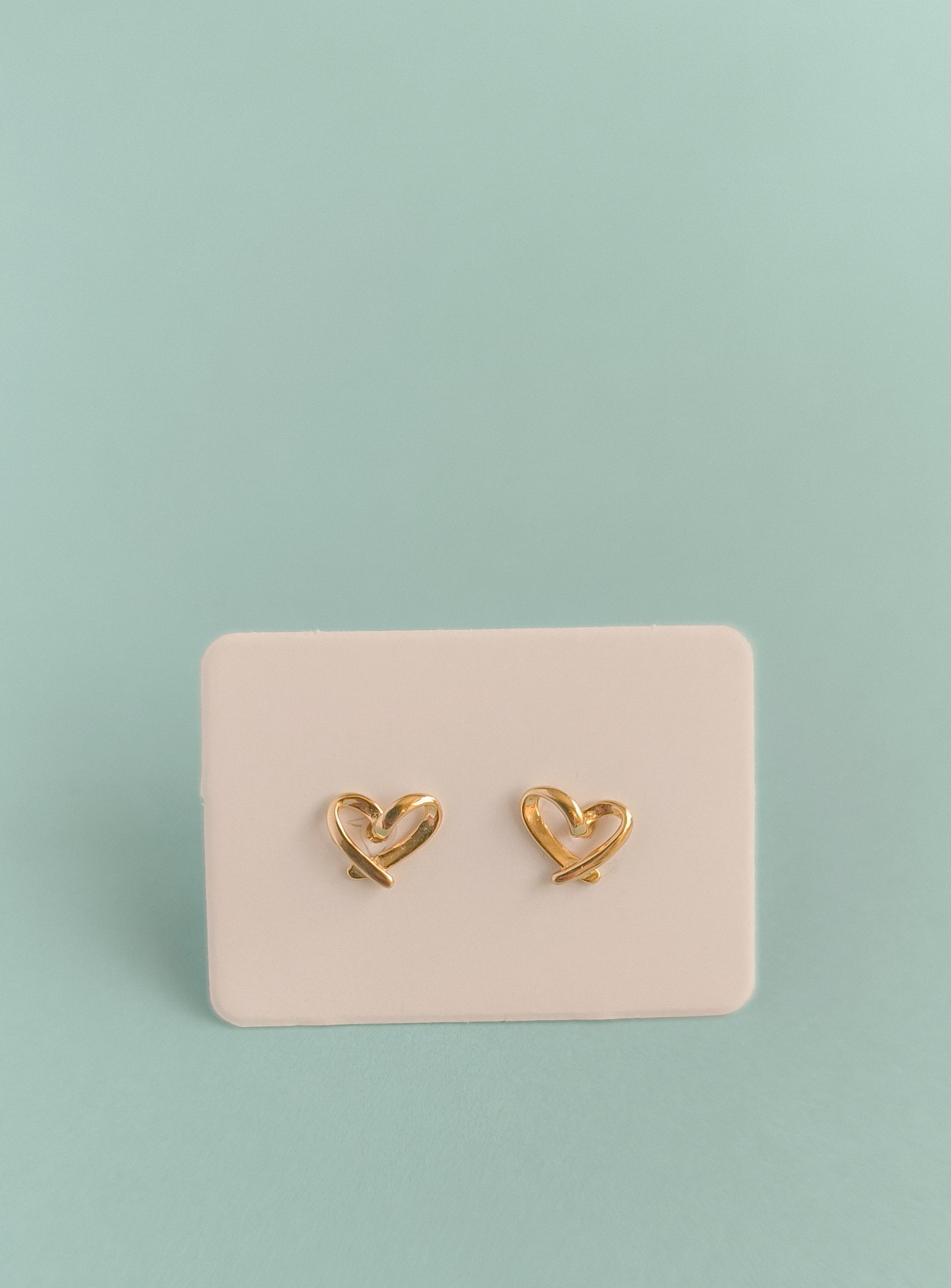 Gold heart-shaped earrings on a pink card against a light green background