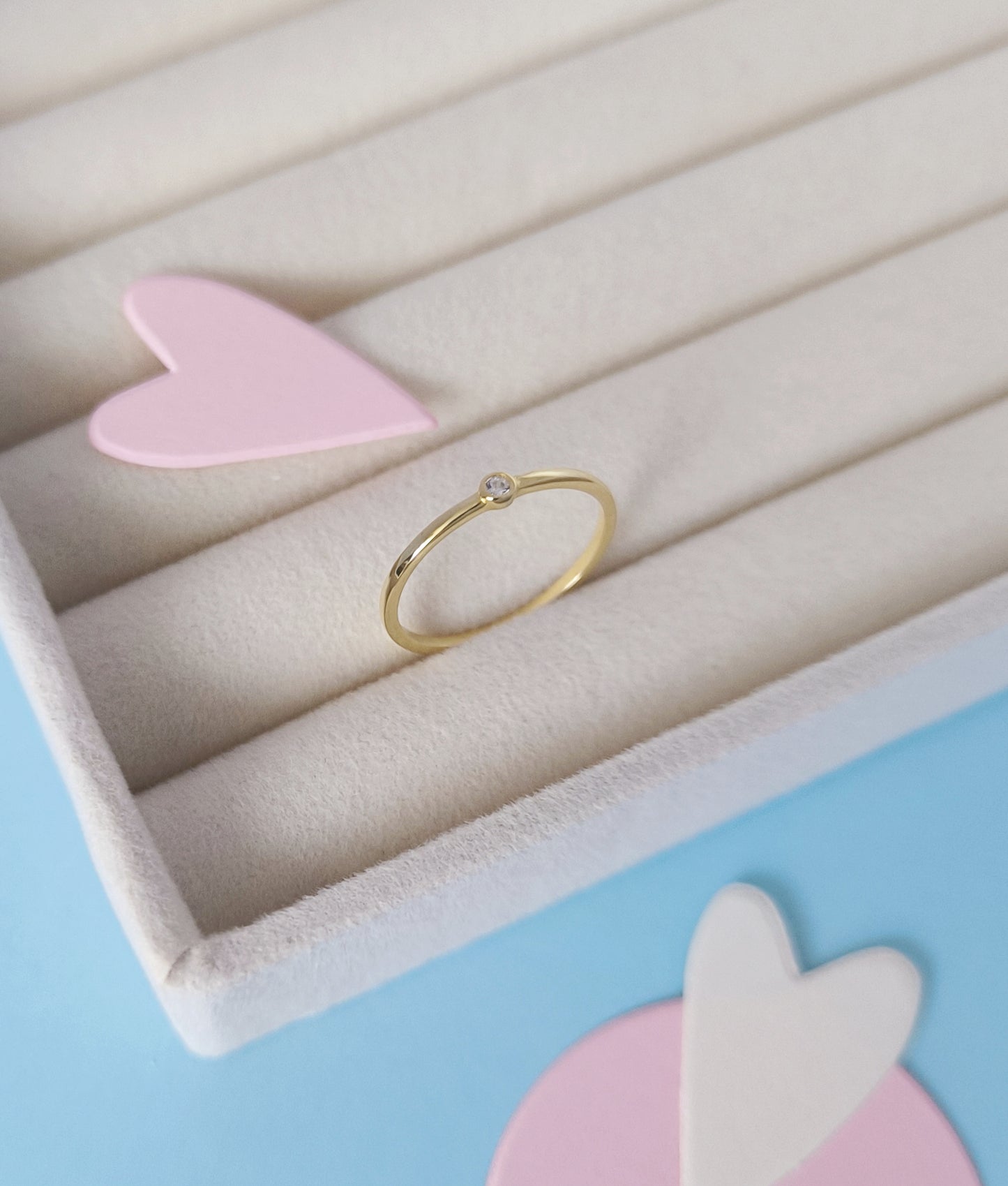 Gold ring on a light pink stand with a soft pastel background