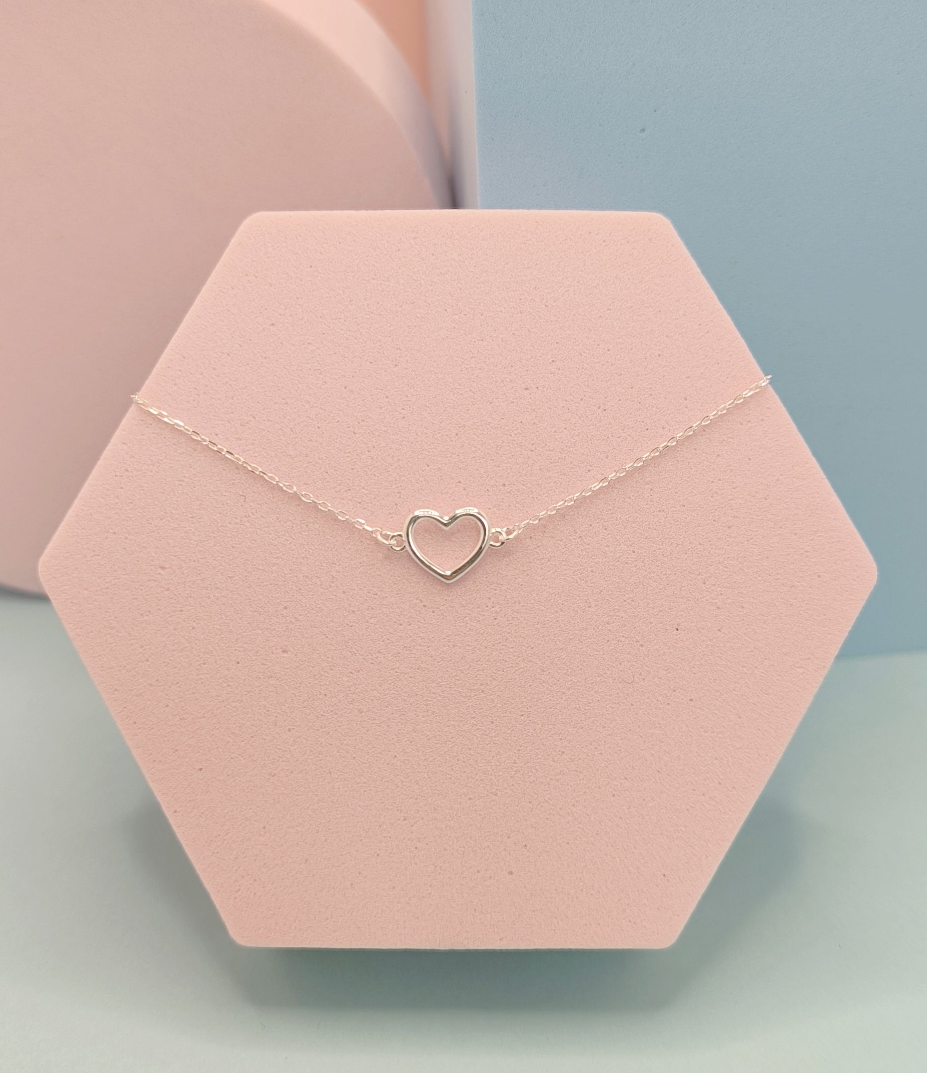 Heart-shaped necklace on a pink hexagonal stand with a light blue background