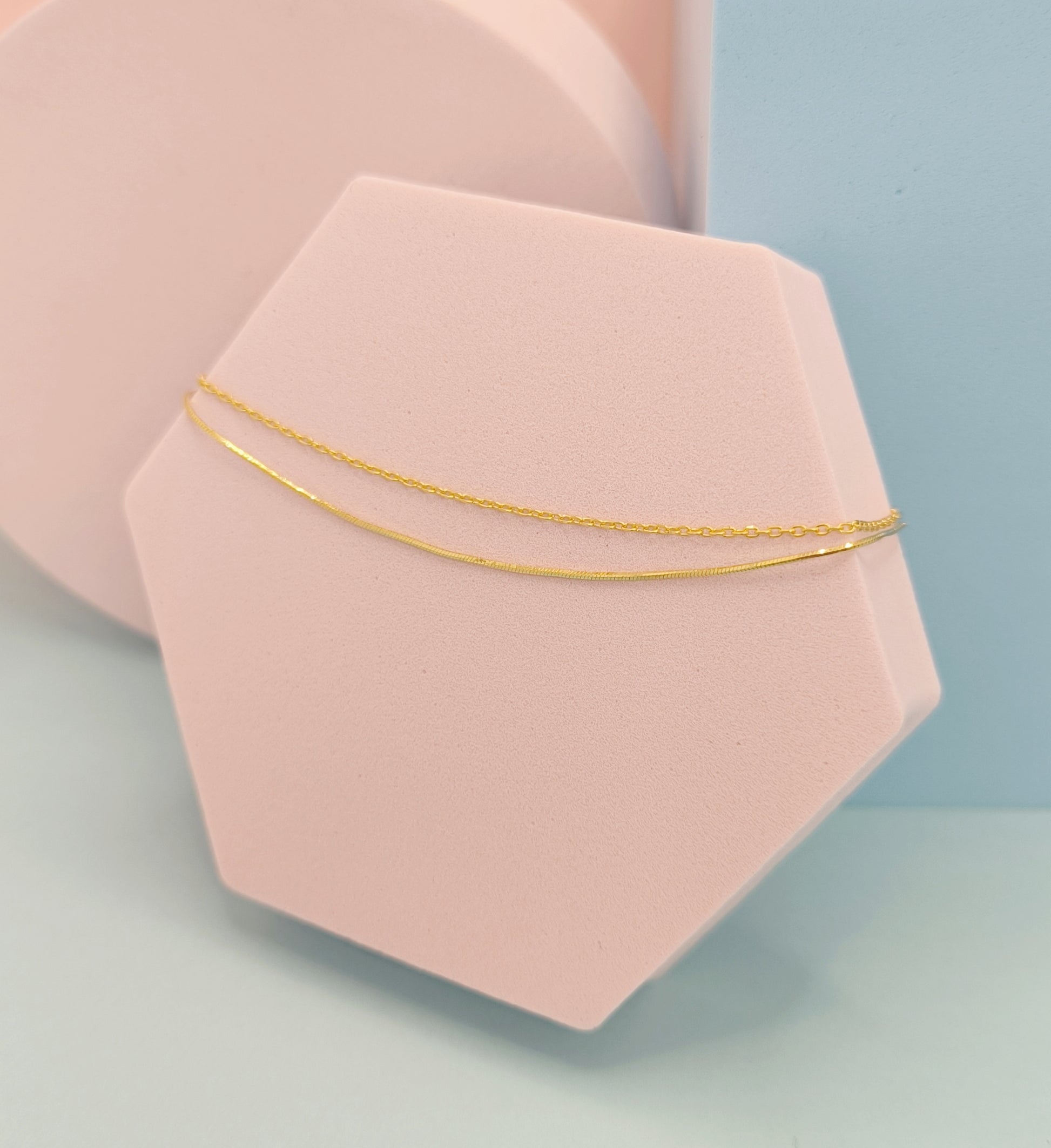Gold bracelet on a pink geometric stand with a light blue background
