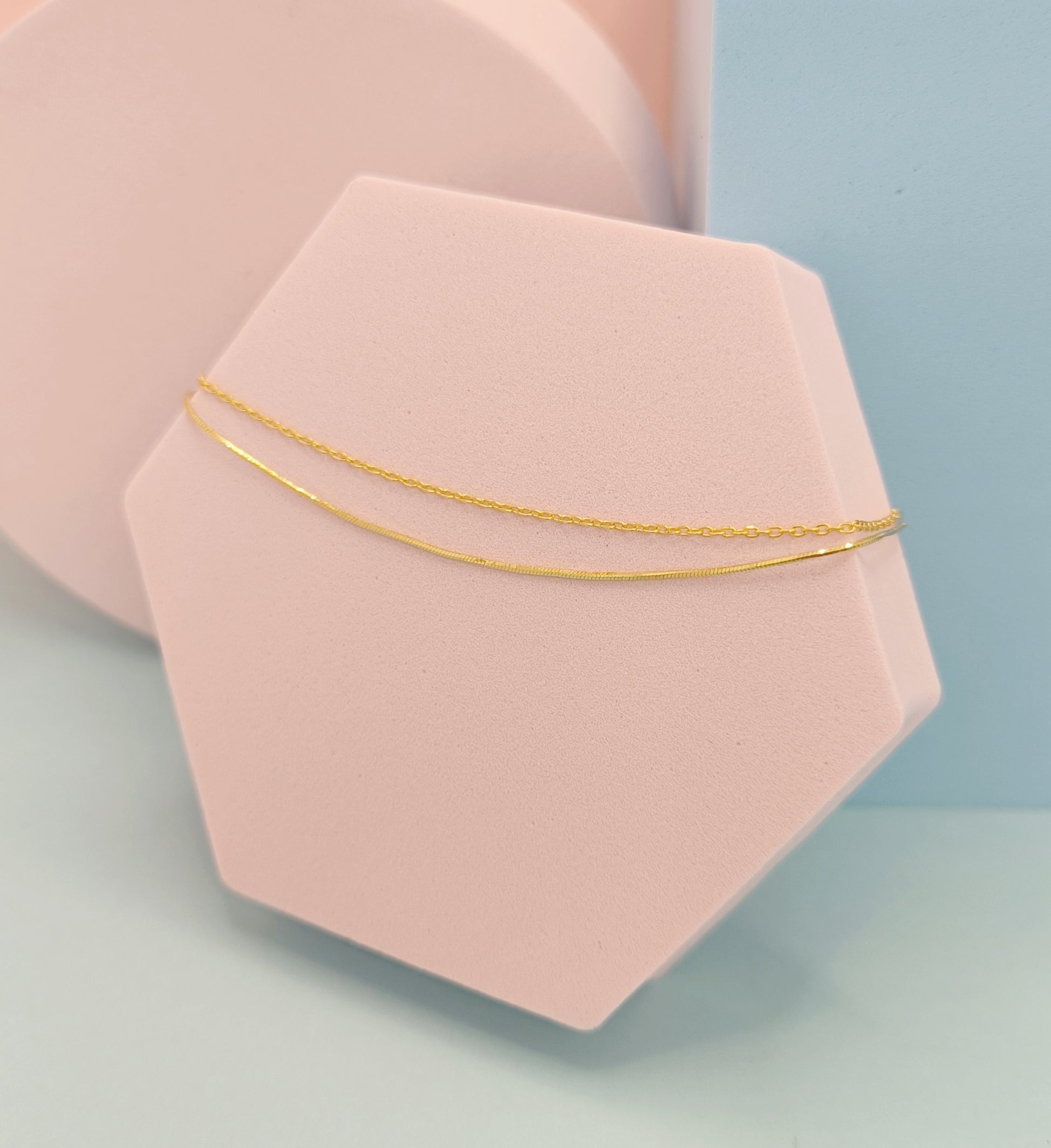 Gold bracelet on a pink geometric stand with a light blue background