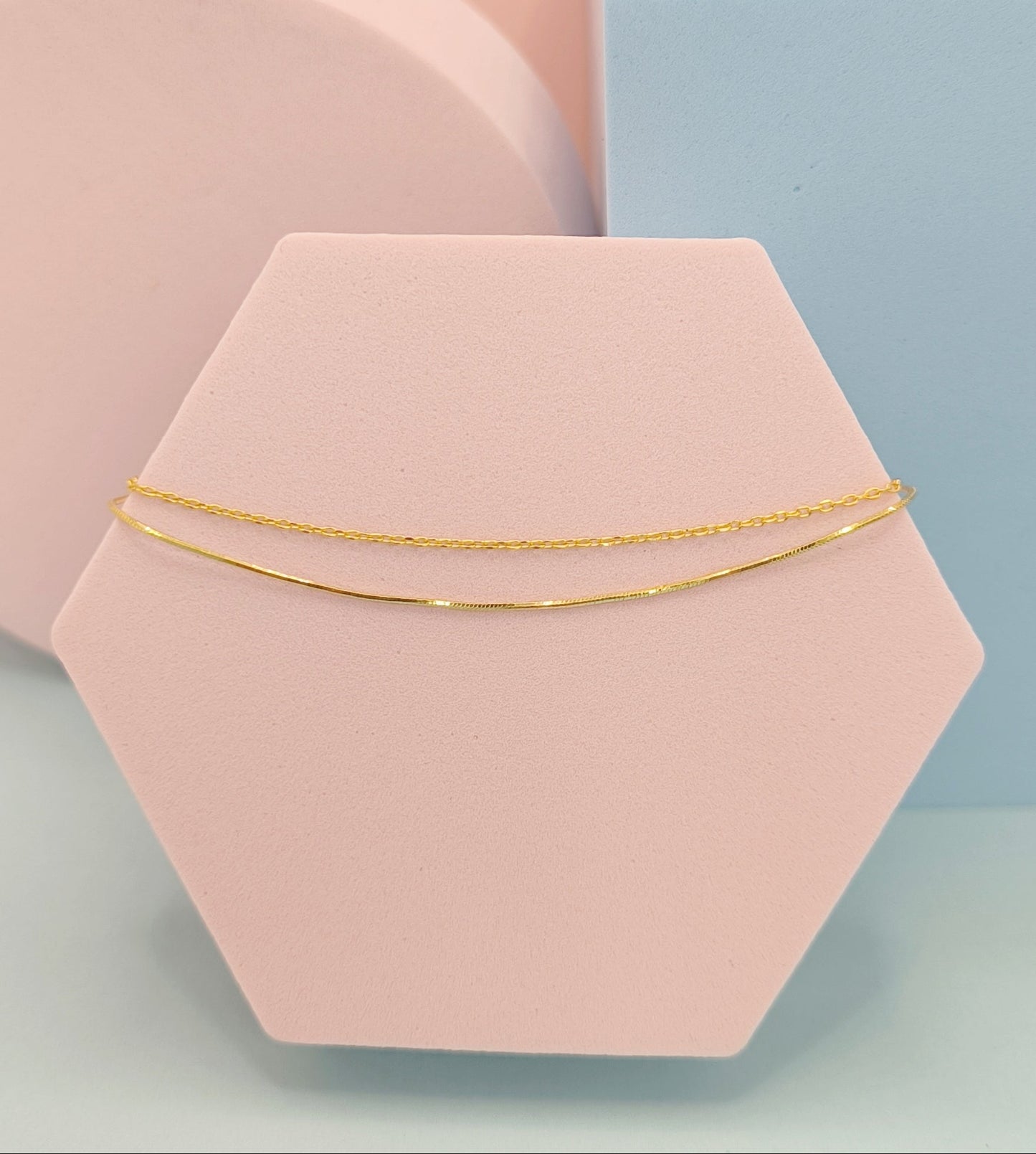 Gold bracelet on a pink hexagonal stand with a geometric background