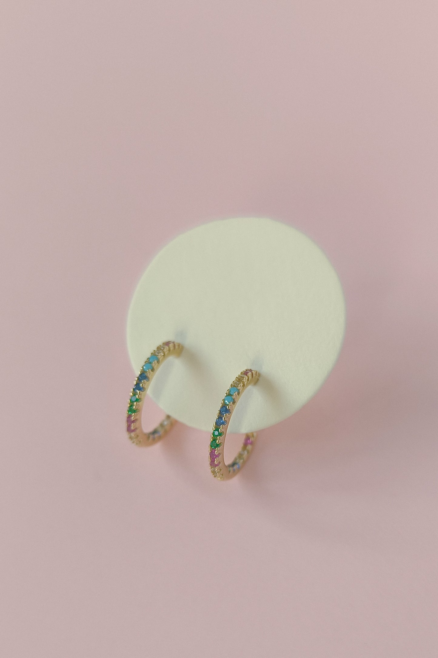 Gold hoop earrings with colorful stones on a pink background
