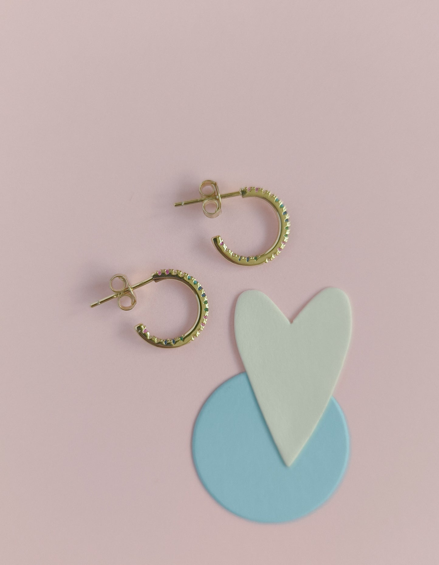 Gold hoop earrings with a heart and circle design on a pink background