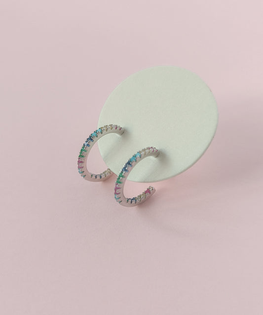 Crescent moon-shaped earrings with colorful stones on a pink background