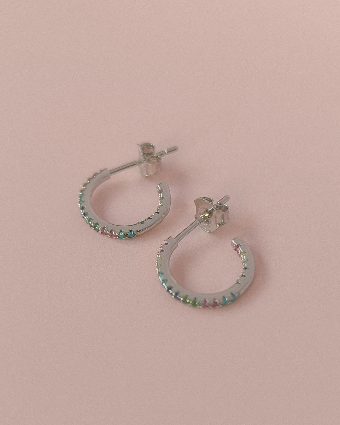 Silver hoop earrings with colorful gemstones on a pink background
