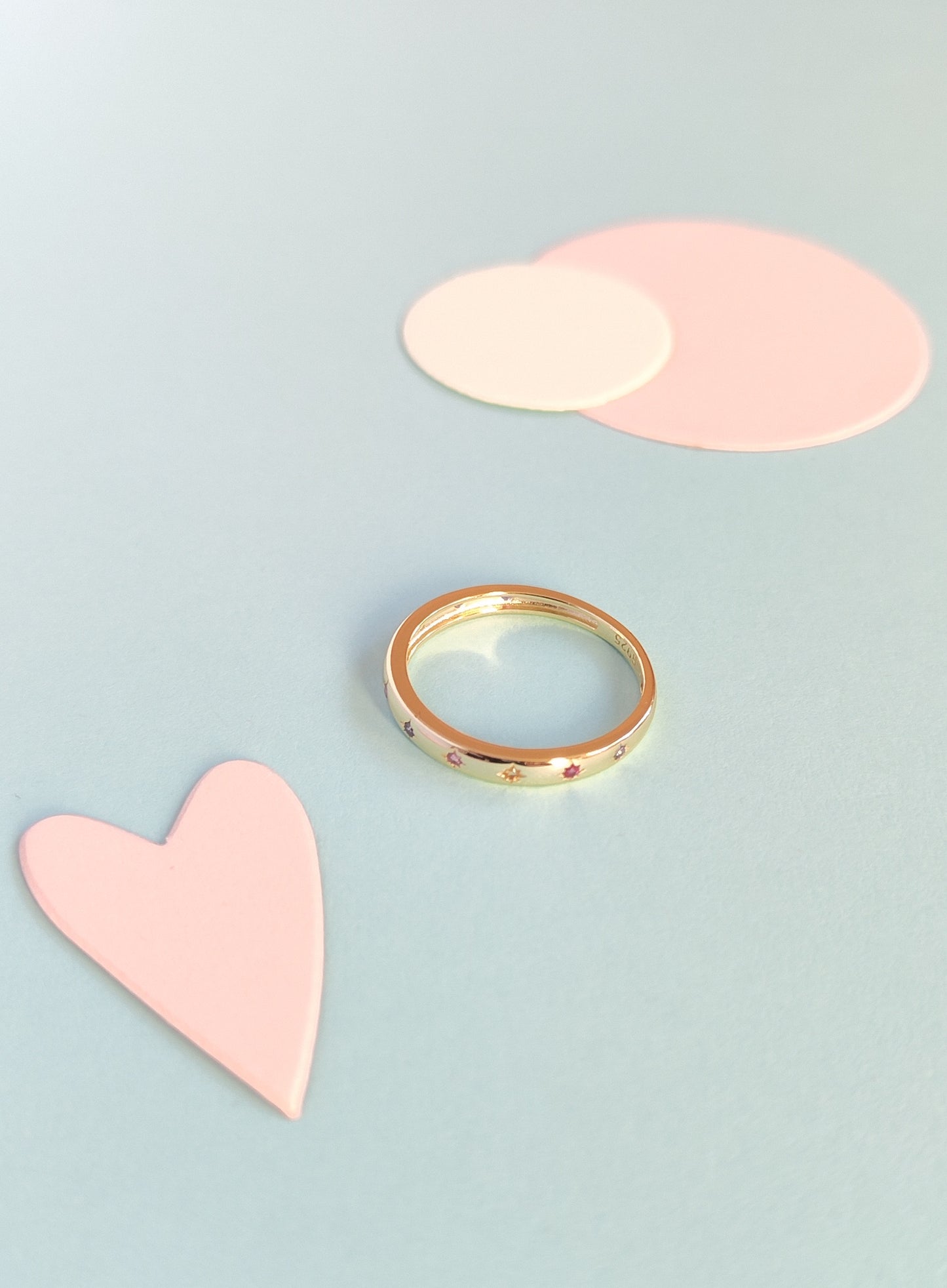 Gold ring on a light blue background with pink heart and circle shapes.