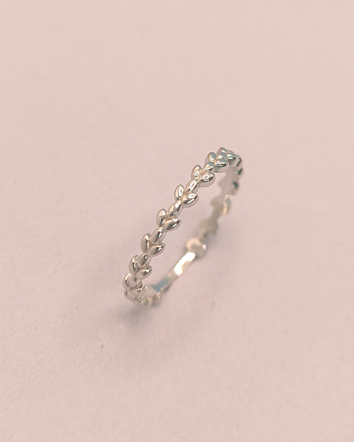 Silver ring with leaf design on a light pink background