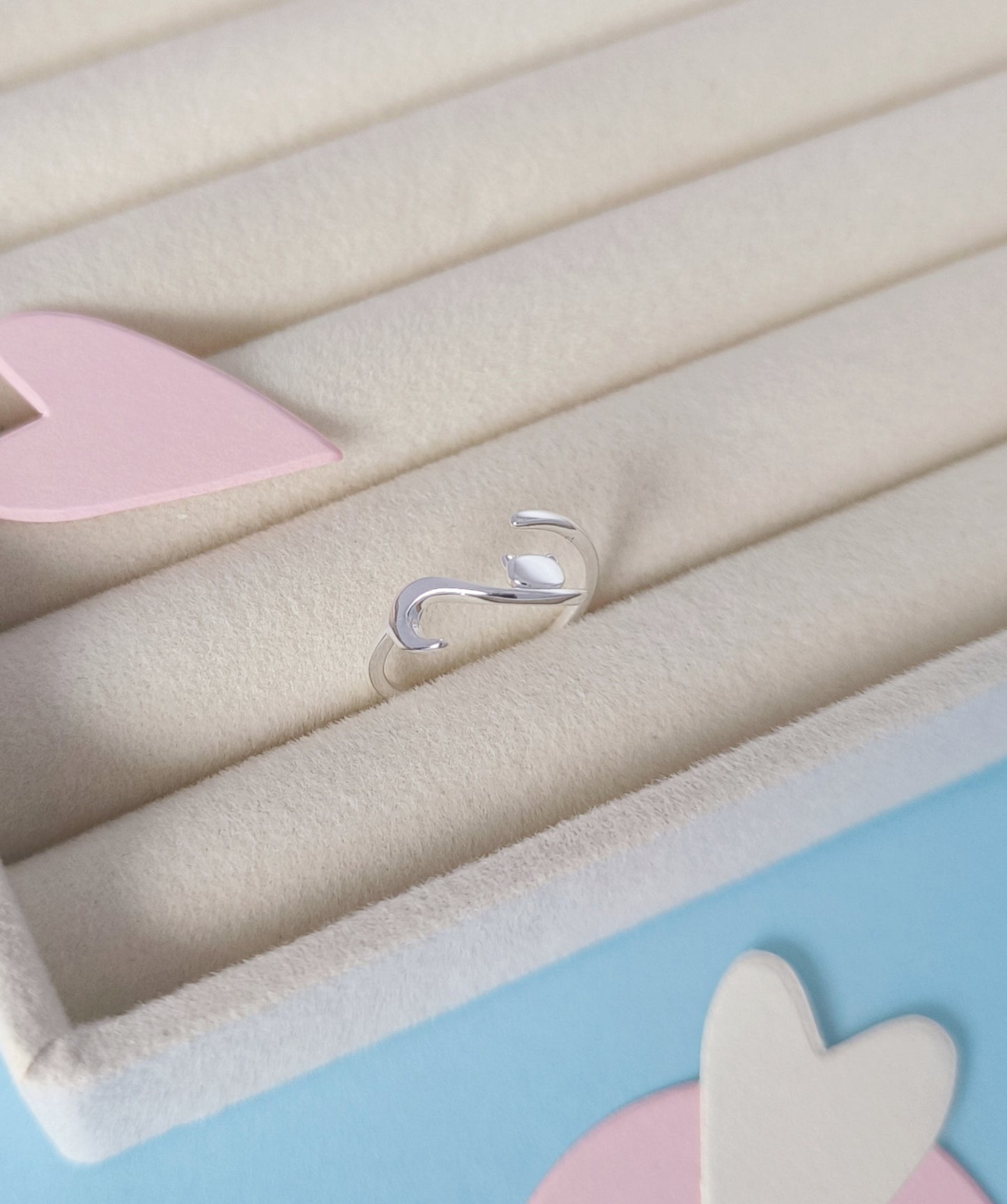 Silver ring on a light blue background with pink and white heart shapes.