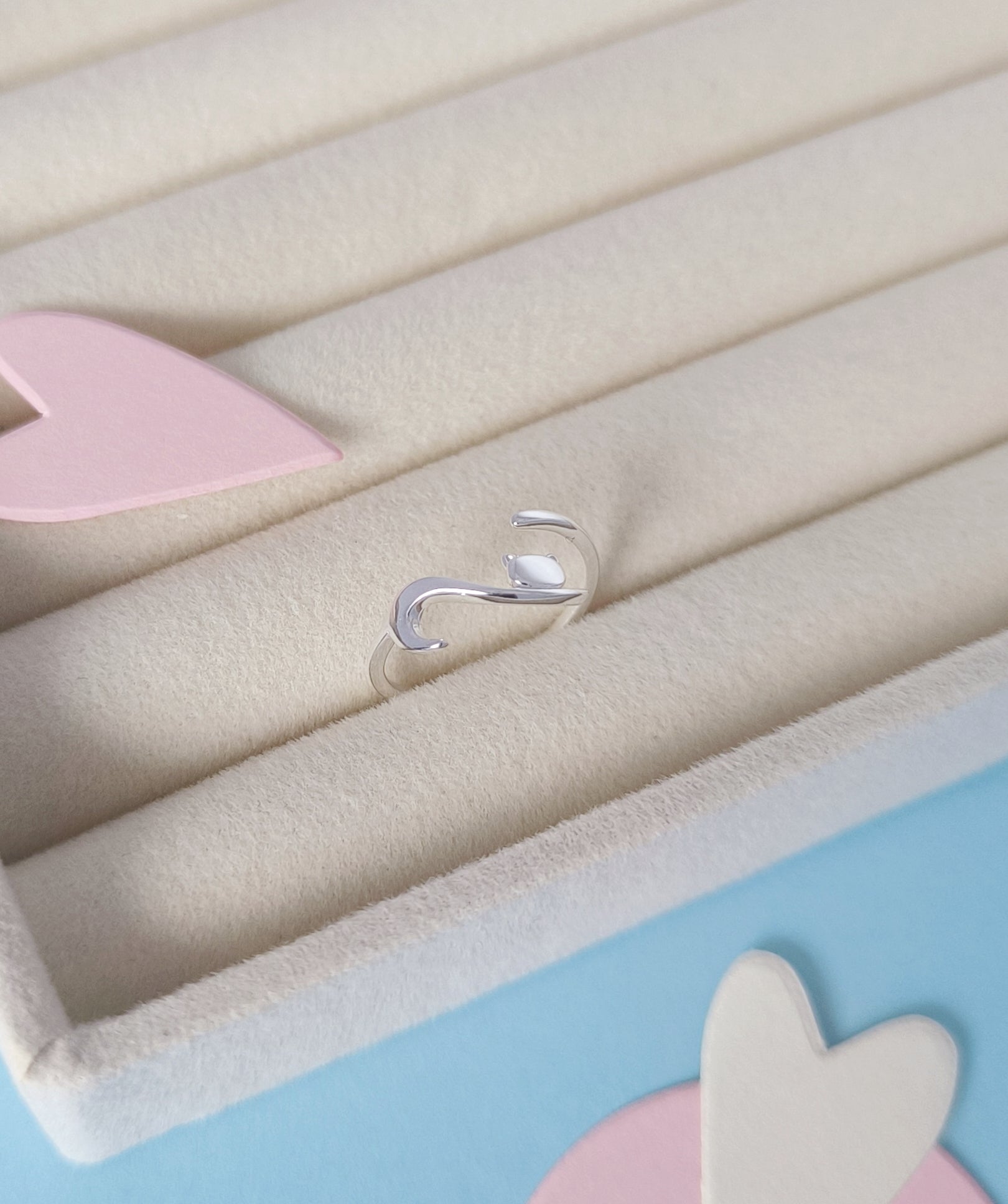 Silver ring on a light blue background with pink and white heart shapes.