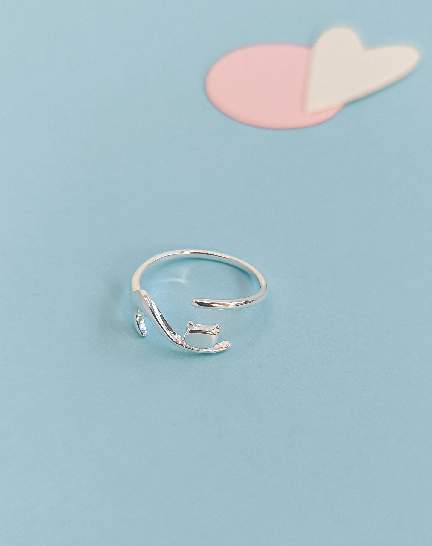 Silver ring on a light blue background with pink and white heart shapes.