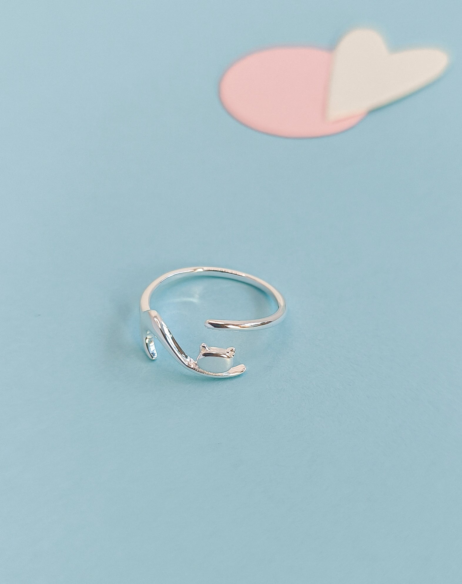 Silver ring on a light blue background with pink and white heart shapes.