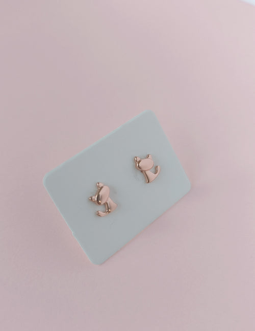 Rose gold cat-shaped earrings on a light blue card with a pink background