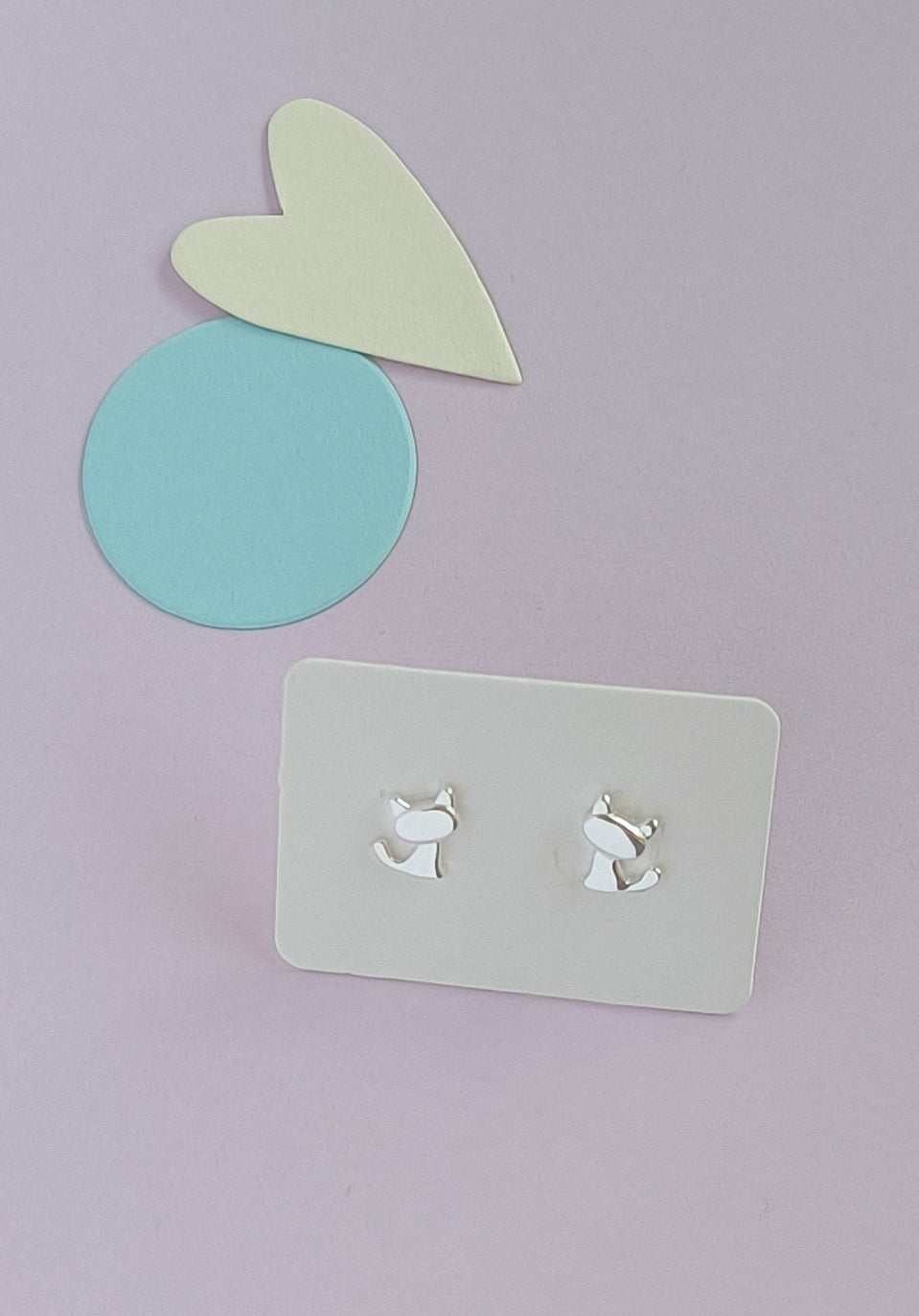 Silver dog-shaped earrings on a gray card with a light purple background