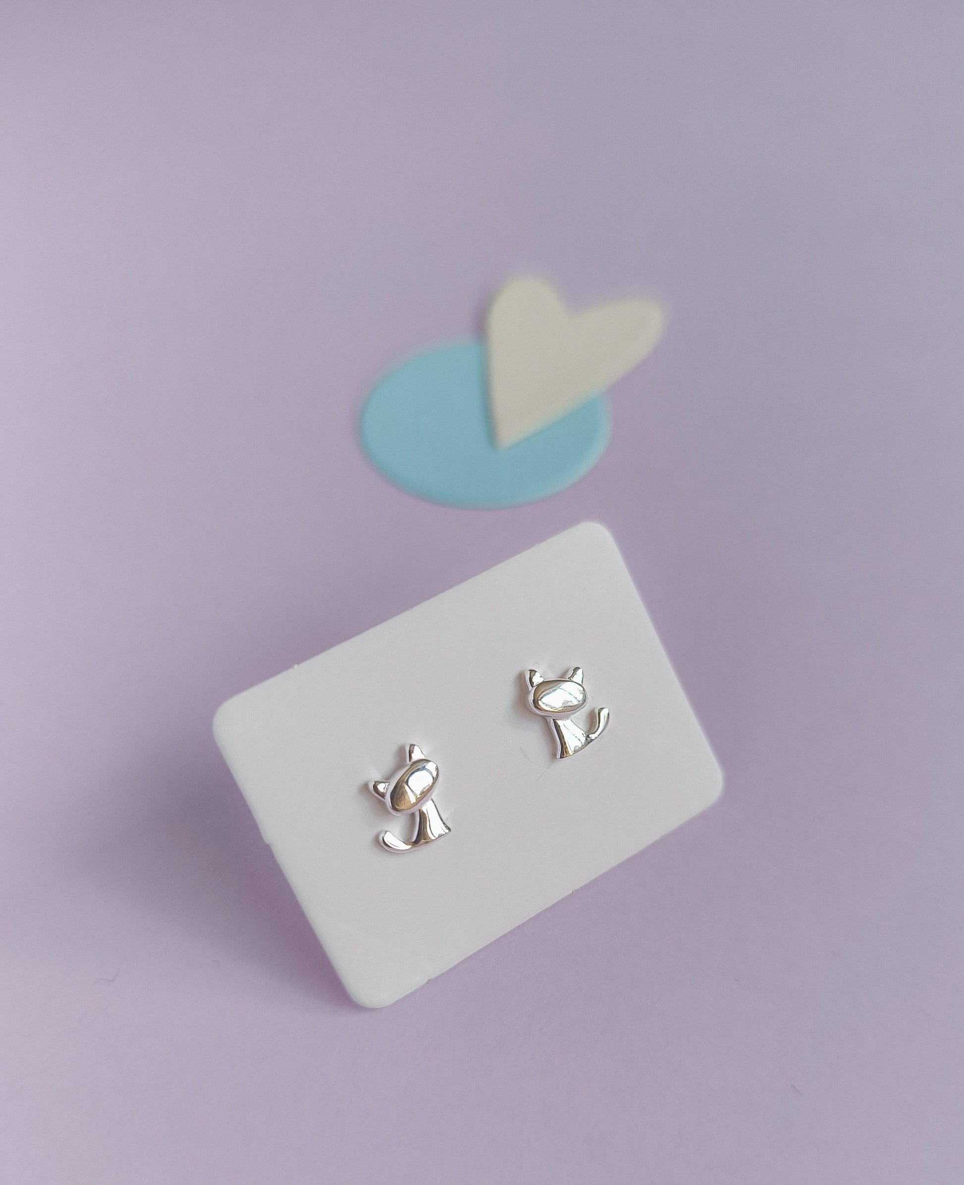 Silver cat-shaped earrings on a white card with a purple background