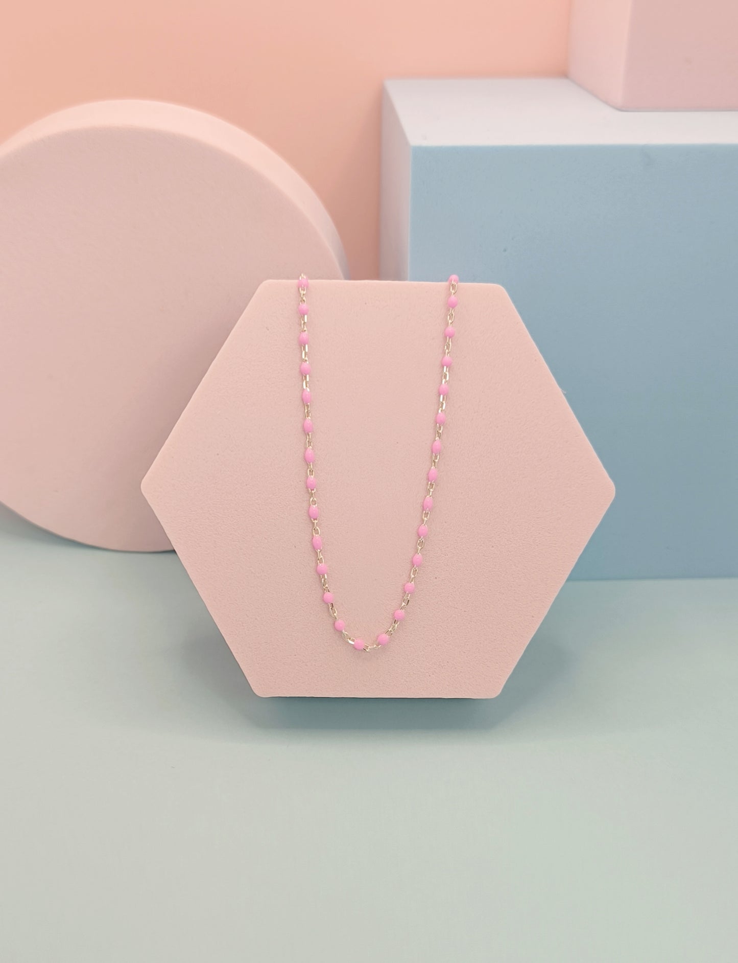 Pink beaded necklace on a hexagonal pink stand against a pastel background